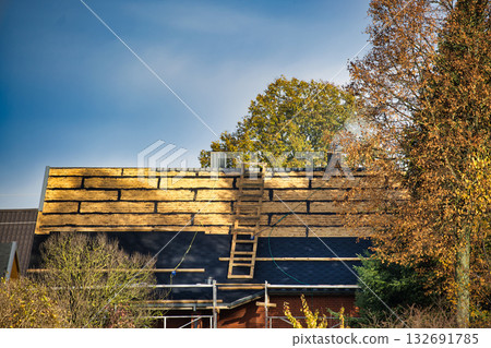 Roof Under Construction With Wooden Planks, Ladder And Autumn Trees Under Clear Blue Sky Roof Under Construction With Wooden Planks, Ladder And Autumn Trees Under Clear Blue Sky 132691785