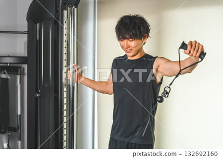 一名年輕的亞洲男子正在健身房使用滑輪機進行肩部運動。 132692160
