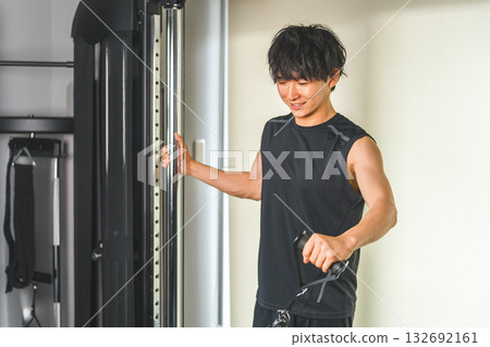 一名年輕的亞洲男子正在健身房使用滑輪機進行肩部運動。 132692161