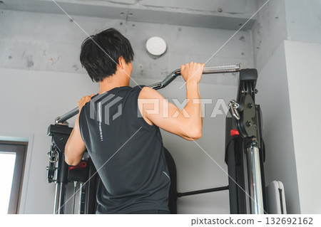 Young Asian man doing pull-ups on a chin-up machine at the gym Young Asian man doing pull-ups on a chin-up machine at the gym 132692162