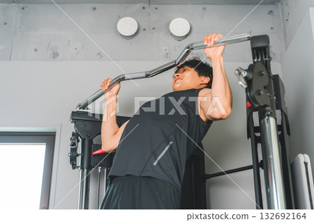 Young Asian man doing pull-ups on a chin-up machine at the gym Young Asian man doing pull-ups on a chin-up machine at the gym 132692164