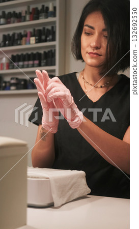 Beautician work. Nail treatment. Woman wearing pink latex medical sterilized protective gloves hands getting ready for manicure procedure. 132692550