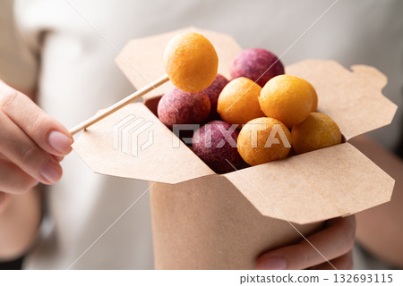 Deep fried sweet potato balls in paper box holding by hand and eating, Thai street food snack Deep fried sweet potato balls in paper box holding by hand and eating, Thai street food snack 132693115