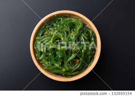 Wakame seaweed salad with sesame seed in a wooden bowl on black background, Top view Wakame seaweed salad with sesame seed in a wooden bowl on black background, Top view 132693154