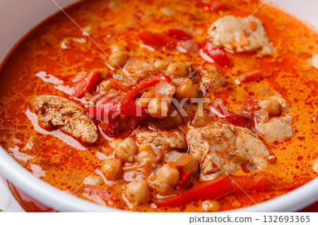 Tikka masala with chicken and chickpeas in red pot. Tikka masala with chicken and chickpeas in red pot. 132693365