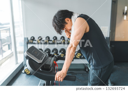 Young Asian man doing aerobic exercise on a walking machine in a sports gym Young Asian man doing aerobic exercise on a walking machine in a sports gym 132693724