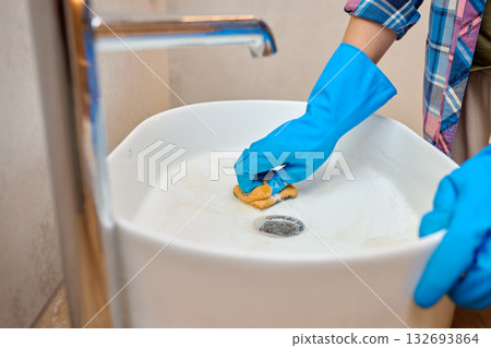 Woman cleaning bathroom sink with sponge and gloves 132693864