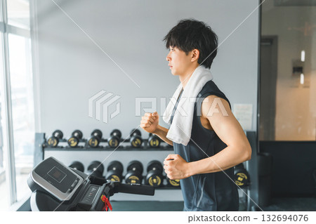 一位年輕的亞洲男子正在健身房的步行機上進行有氧運動（慢跑）。 132694076