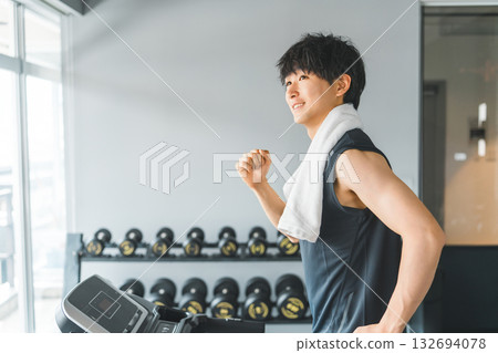 Young Asian man doing aerobic exercise (jogging) on a walking machine in a sports gym Young Asian man doing aerobic exercise (jogging) on a walking machine in a sports gym 132694078