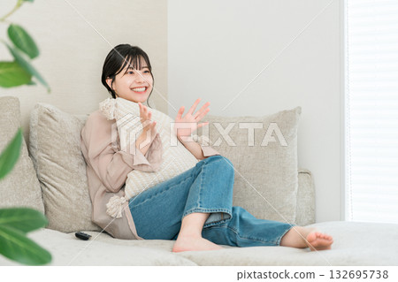 一位年輕的亞洲女性坐在客廳的沙發上看電視或電影。 一位年輕的亞洲女性坐在客廳的沙發上看電視或電影。 132695738