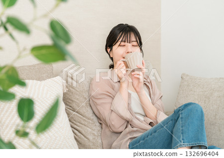 一位放鬆的亞洲女性在家中喝著咖啡、茶或熱水（暖暖身子）。 132696404