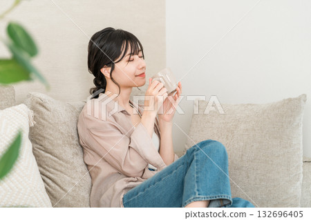 一位放鬆的亞洲女性在家中喝著咖啡、茶或熱水（暖暖身子）。 132696405