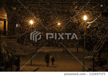 日本的日常生活：一位母親帶著年幼的孩子在雪夜漫步於一座小型城市公園。 132697375