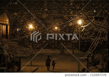 日本的日常生活:一位母親帶著年幼的孩子在雪夜漫步於一座小型城市公園。 日本的日常生活:一位母親帶著年幼的孩子在雪夜漫步於一座小型城市公園。 132697376