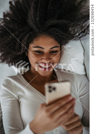Portrait of young woman using smartphone, lying in bed. 132698454