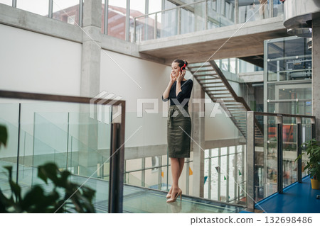 Businesswoman with headphones standing in modern openspace office building. 132698486