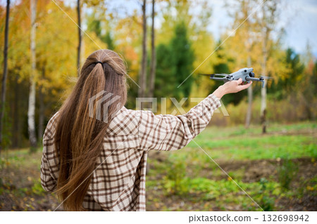 A young person stands in a vibrant forest during autumn, ready to launch a drone into the colorful trees and nature. The scene is peaceful and full of life. 132698942