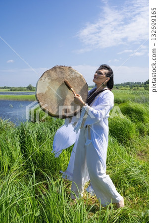 Female shaman in the white dress drumming outdoors Female shaman in the white dress drumming outdoors 132699165