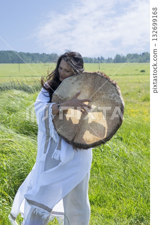 Female shaman in the white dress drumming outdoors Female shaman in the white dress drumming outdoors 132699168