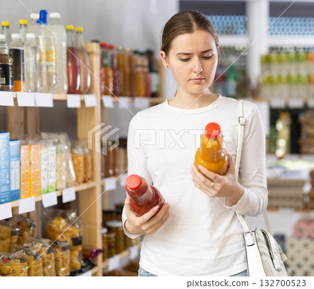 Female shopper chooses peach juice or tomato juice while shopping in supermarket Female shopper chooses peach juice or tomato juice while shopping in supermarket 132700523
