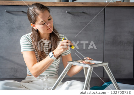 Young woman sitting on the floor assembling a chair with tools. Concept of female independence and do it yourself lifestyle. 132700728