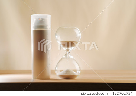 A modern still life featuring skincare product with an hourglass, embodying timeless beauty and minimalism. A focus on creativity and elegance in self-care displayed on a serene, neutral backdrop. 132701734