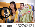 Two young asian woman live streaming online clothing store while showing clothing with smartphone. 132702421