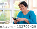 Senior asian woman smile while using on smartphone sitting on sofa in living room at home. 132702429