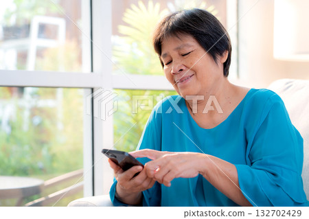 Senior asian woman smile while using on smartphone sitting on sofa in living room at home. Senior asian woman smile while using on smartphone sitting on sofa in living room at home. 132702429