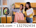 Two asian woman live streaming online clothing store while showing clothing with smartphone. 132702434