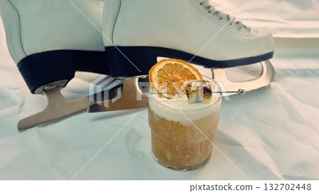 Cocktail with toasted marshmallow and dried orange near white ice skates Cocktail with toasted marshmallow and dried orange near white ice skates 132702448