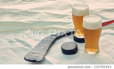 Two glasses of beer near hockey stick and puck on white background Two glasses of beer near hockey stick and puck on white background 132702452