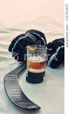 Whiskey glass with orange zest near hockey gloves and stick on white surface 132702455