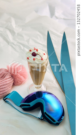 Glass of coffee with whipped cream cherry and ski goggles on snow 132702458