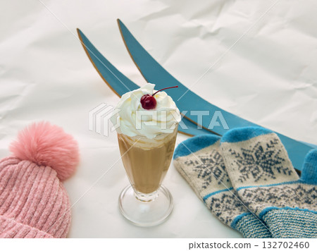 Coffee with whipped cream and cherry beside pink hat blue mittens and skis 132702460