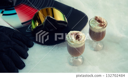 Two hot drinks with whipped cream and snowboard gear on snow surface Two hot drinks with whipped cream and snowboard gear on snow surface 132702484