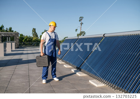 Technician in blue overalls inspecting solar panels on rooftop Technician in blue overalls inspecting solar panels on rooftop 132703225