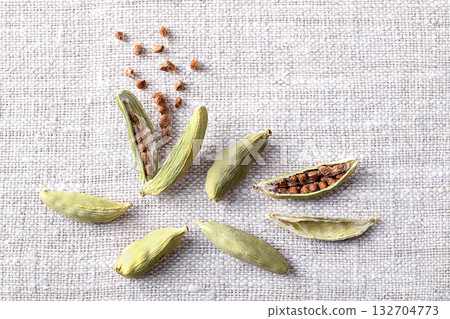 Dried cardamom pods with seeds, close-up, on linen. Light green fruits of Elettaria cardamomum, spindle shaped seed pods, with papery outer shell, and small seeds. Spice with strong and punchy aroma. Dried cardamom pods with seeds, close-up, on linen. Light green fruits of Elettaria cardamomum, spindle shaped seed pods, with papery outer shell, and small seeds. Spice with strong and punchy aroma. 132704773