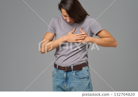 Woman holding chest with both hands, bending forward in pain, neutral background Woman holding chest with both hands, bending forward in pain, neutral background 132704820