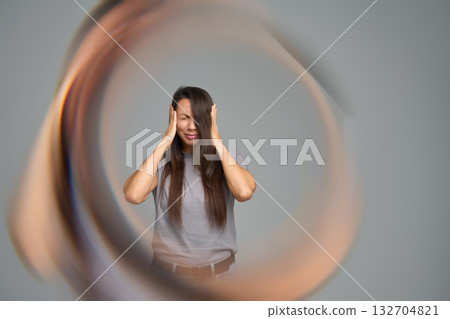 Woman holding head in pain surrounded by circular distortion symbolizing migraine or tinnitus Woman holding head in pain surrounded by circular distortion symbolizing migraine or tinnitus 132704821