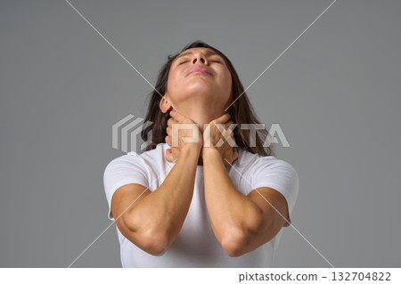 Woman holding neck in pain and looking up showing tension or discomfort in throat area indoors Woman holding neck in pain and looking up showing tension or discomfort in throat area indoors 132704822