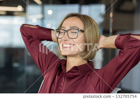 Happy businesswoman relaxing with hands behind head, smiling confidently and feeling satisfied during a break in a modern office, representing work-life balance and job satisfaction Happy businesswoman relaxing with hands behind head, smiling confidently and feeling satisfied during a break in a modern office, representing work-life balance and job satisfaction 132705754