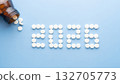 Happy New Year banner for medical theme. Number 2026 made by white pills spilling out of brown glass bottle on blue background. Creative idea for health care, medical and pharmacy concept. 132705773