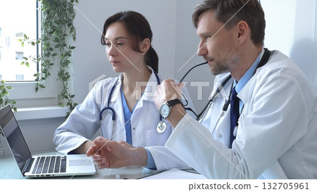Two doctors are studying medical charts on a laptop, discussing patient data in a hospital or clinical setting. Medicine and healthcare concept. 132705961