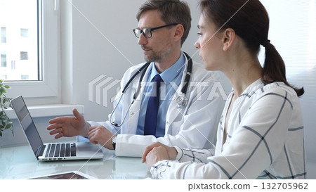 Male doctor showing medical test results on a laptop to a female patient, discussing diagnosis and treatment options in a bright medical office. Medicine and health care Male doctor showing medical test results on a laptop to a female patient, discussing diagnosis and treatment options in a bright medical office. Medicine and health care 132705962