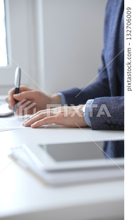 Close up of businessman's hands signing a contract with elegant pen, wearing a blue suit and a wristwatch, sitting at a white desk. Business people concept 132706009