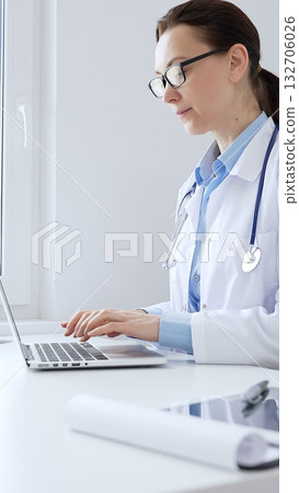 Female doctor is typing on a laptop in a bright medical office, showcasing healthcare technology and medical documentation. Medicine and health care concept Female doctor is typing on a laptop in a bright medical office, showcasing healthcare technology and medical documentation. Medicine and health care concept 132706026