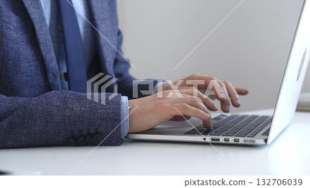 Close up of businessman's hands typing on laptop keyboard, working diligently in a modern office setting, wearing a suit and watch. Business people concept 132706039