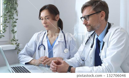 Two doctors are examining medical records on a laptop, engaging in a focused discussion about patient data within a hospital or clinical setting. Medicine and health care concept Two doctors are examining medical records on a laptop, engaging in a focused discussion about patient data within a hospital or clinical setting. Medicine and health care concept 132706046