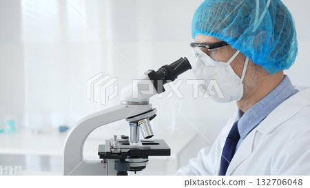 Experienced scientist examining microscopic sample, wearing full protective gear inside sterile research laboratory. Health care and science concept 132706048